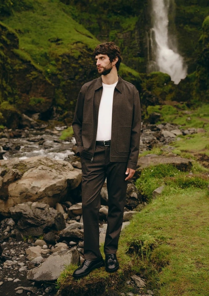 Matthew Bell wears a dark jacket over a white T-shirt and dark trousers beside a waterfall.