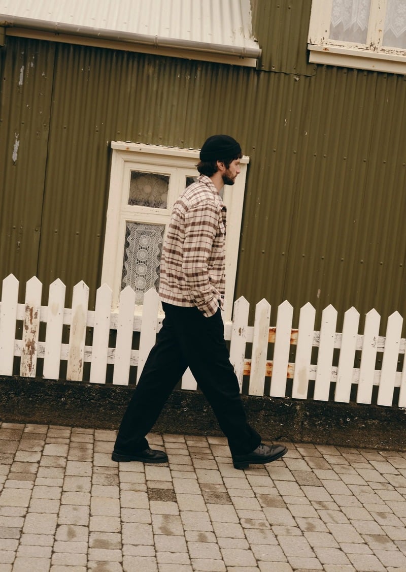 Matthew Bell walks past a picket fence in a checked jacket and dark trousers.