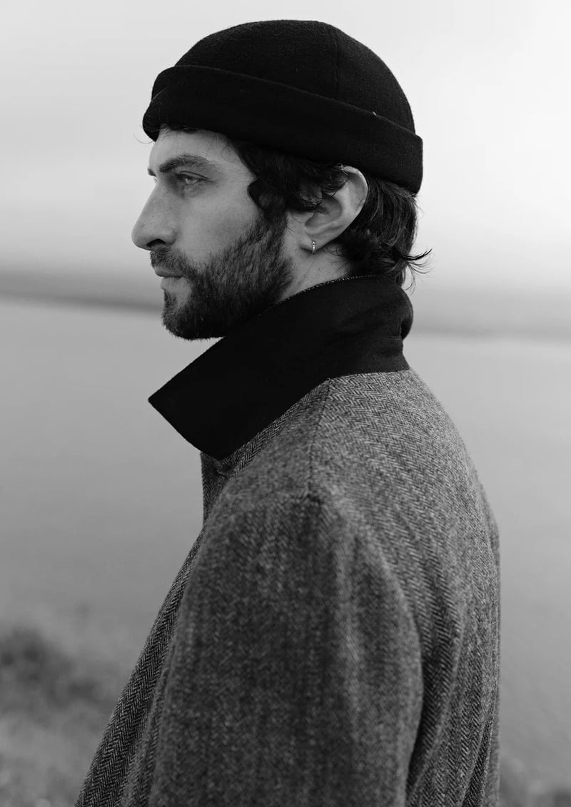 Matthew Bell wears a beanie and a raised coat collar in a black-and-white profile portrait.