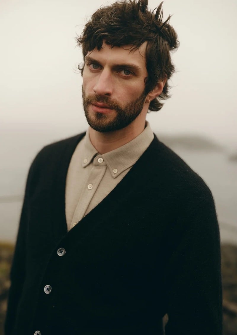 Matthew Bell wears a black cardigan over a pale button-down shirt in an outdoor portrait.
