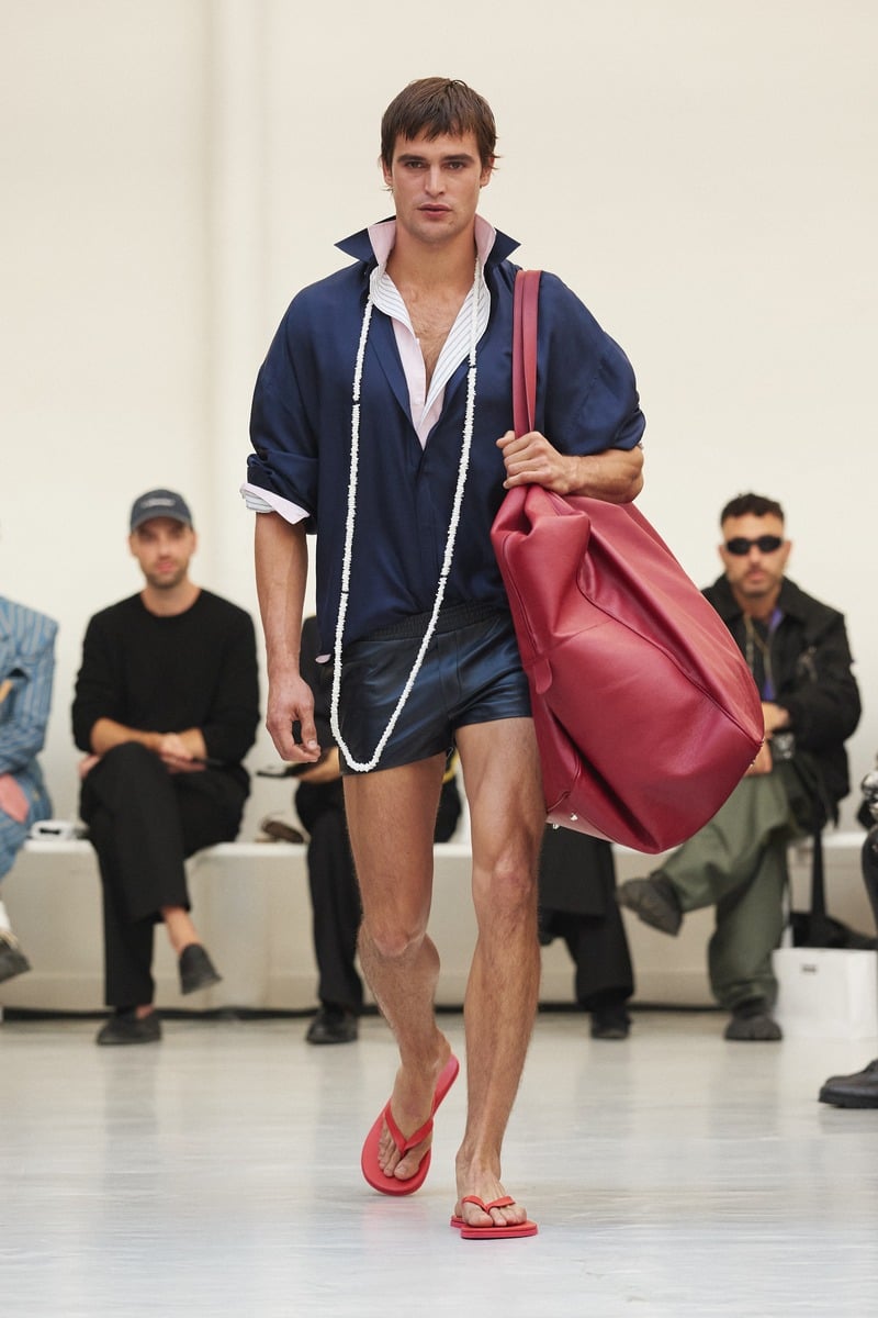 Parker van Noord carrying an oversized red bag with a navy top, short shorts and red flip-flops at Situationist spring-summer 2027.