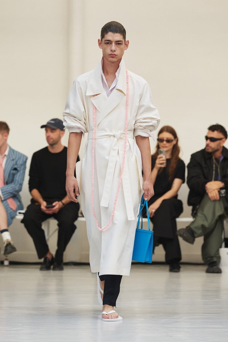 Model wearing a belted white coat and carrying a blue bag at Situationist spring-summer 2027.