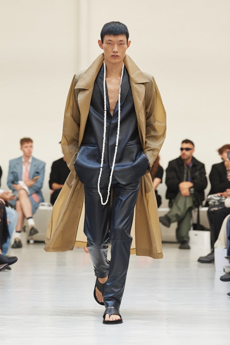 Model wearing a tan coat over a dark open-neck outfit with a long necklace at Situationist spring-summer 2027.