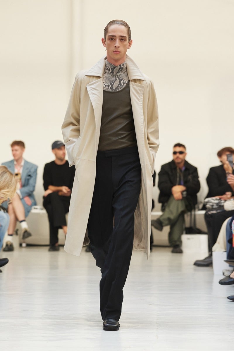 Model wearing a light coat with dark trousers and a patterned neck detail at Situationist spring-summer 2027.