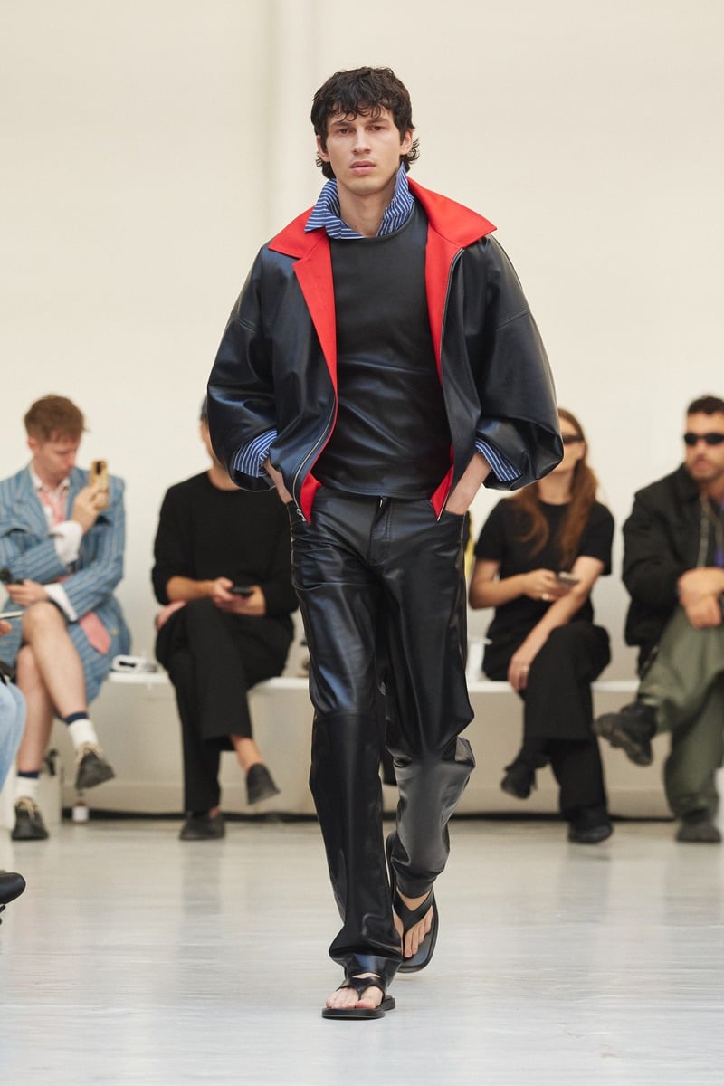 Model wearing a dark jacket with a red collar, striped shirt and leather trousers at Situationist spring-summer 2027.