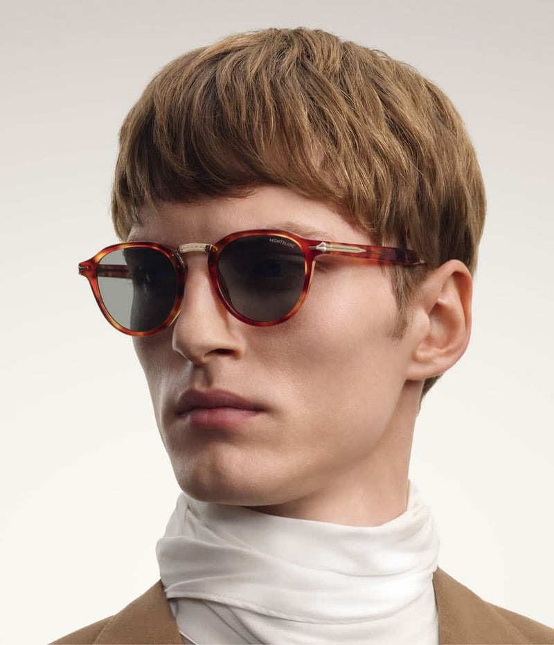 Tammo Rahming wears rounded tortoiseshell Montblanc sunglasses with a metal bridge, a white scarf, and a camel jacket.