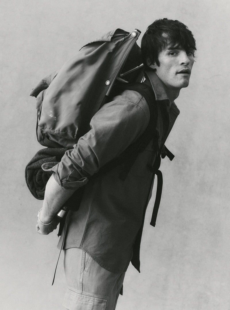 Black-and-white portrait of a model wearing a button-down shirt and a backpack. Taylor Stitch winter 2026 collection.