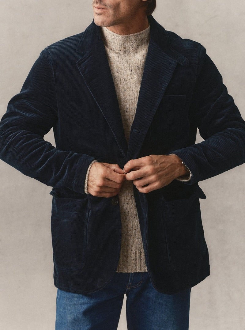 Close-up of a model buttoning a navy corduroy sportcoat over a pale rollneck sweater. Taylor Stitch winter 2026 collection.