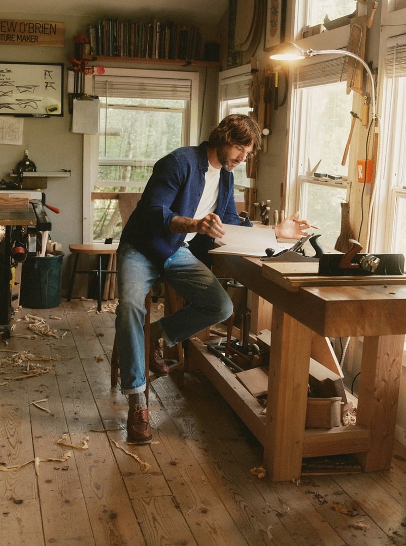 Man wearing an indigo shirt while working at a wooden workshop table. Taylor Stitch winter 2026 collection.