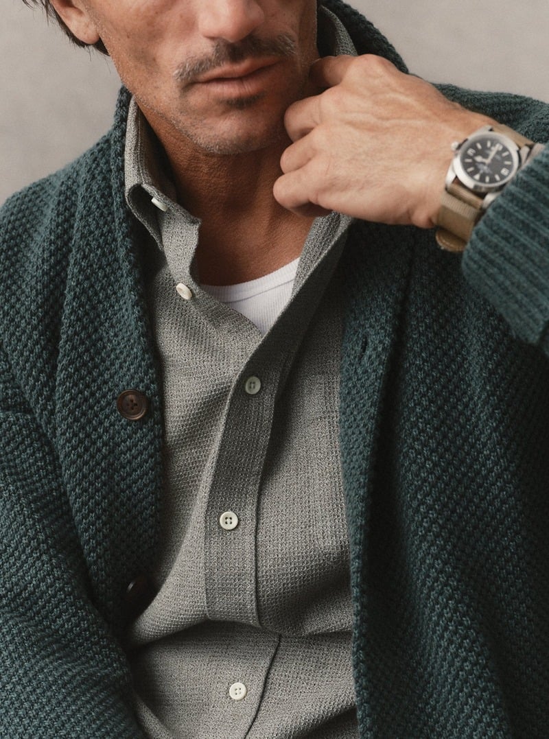 Close-up of a dark green textured cardigan layered over a gray button-down shirt. Taylor Stitch winter 2026 collection.
