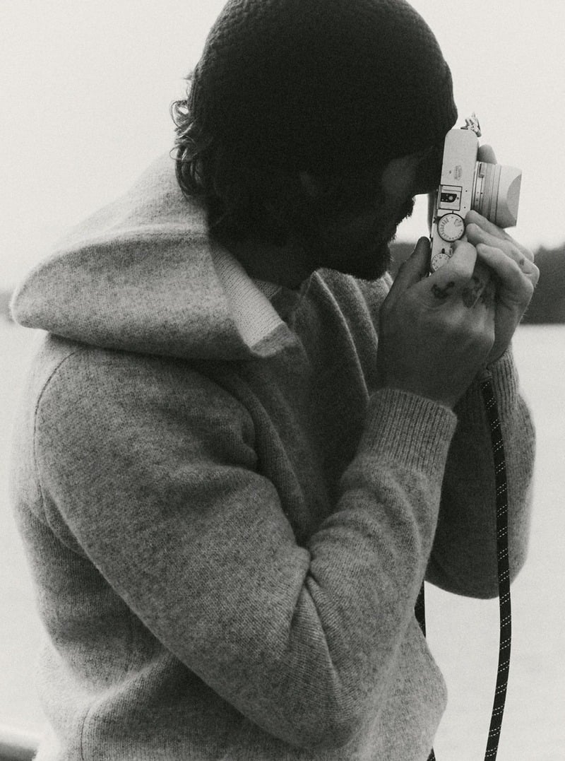 Black-and-white photograph of a model wearing a sweater hoodie while taking a photograph. Taylor Stitch winter 2026 collection.