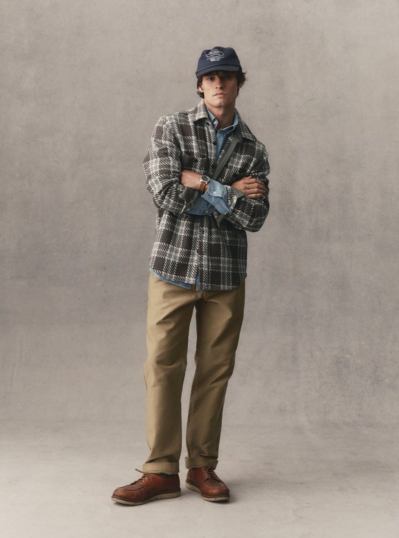 Model wearing a plaid overshirt over a button-down shirt with tan trousers. Taylor Stitch winter 2026 collection.
