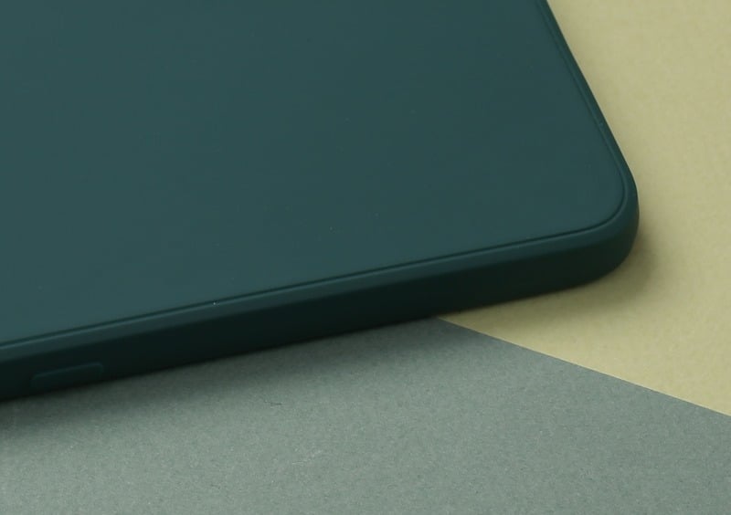 Close-up of a green silicone phone case showing its bottom corner and edge on a two-tone surface.
