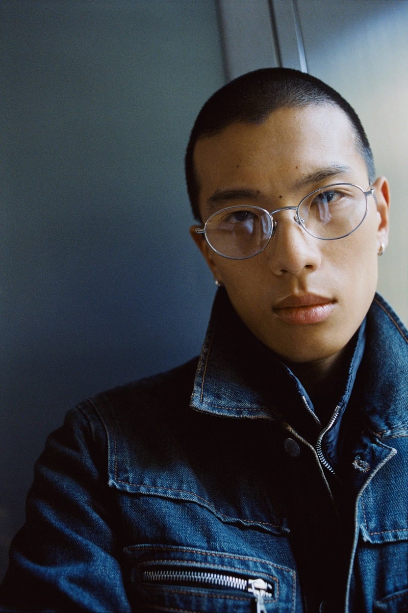 Yuyang Cai wears silver metal glasses and a denim jacket in a close-up for THISTLES.