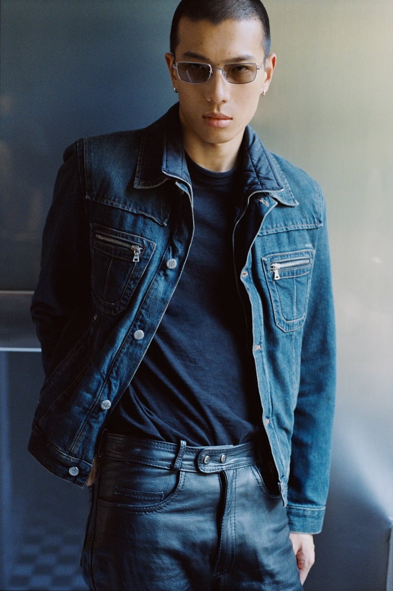 Yuyang Cai wears transparent glasses with a denim jacket, dark shirt, and jeans.