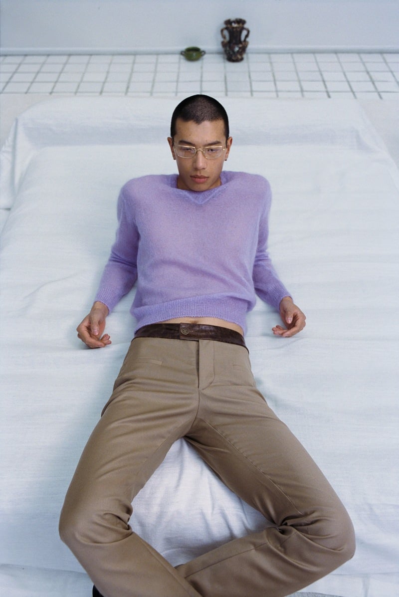 Yuyang Cai reclines wearing a lavender sweater and tan trousers.