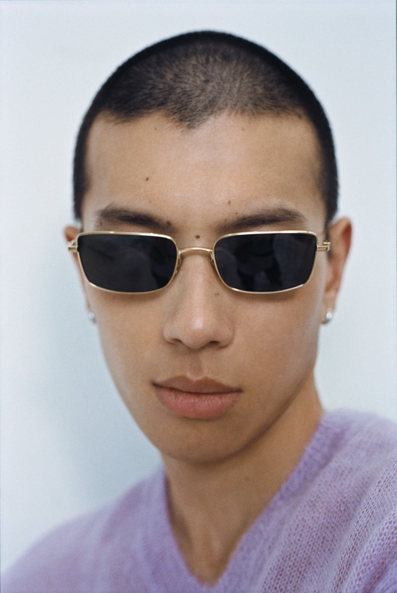 Yuyang Cai wears rectangular metal sunglasses and a lavender sweater in a close-up.