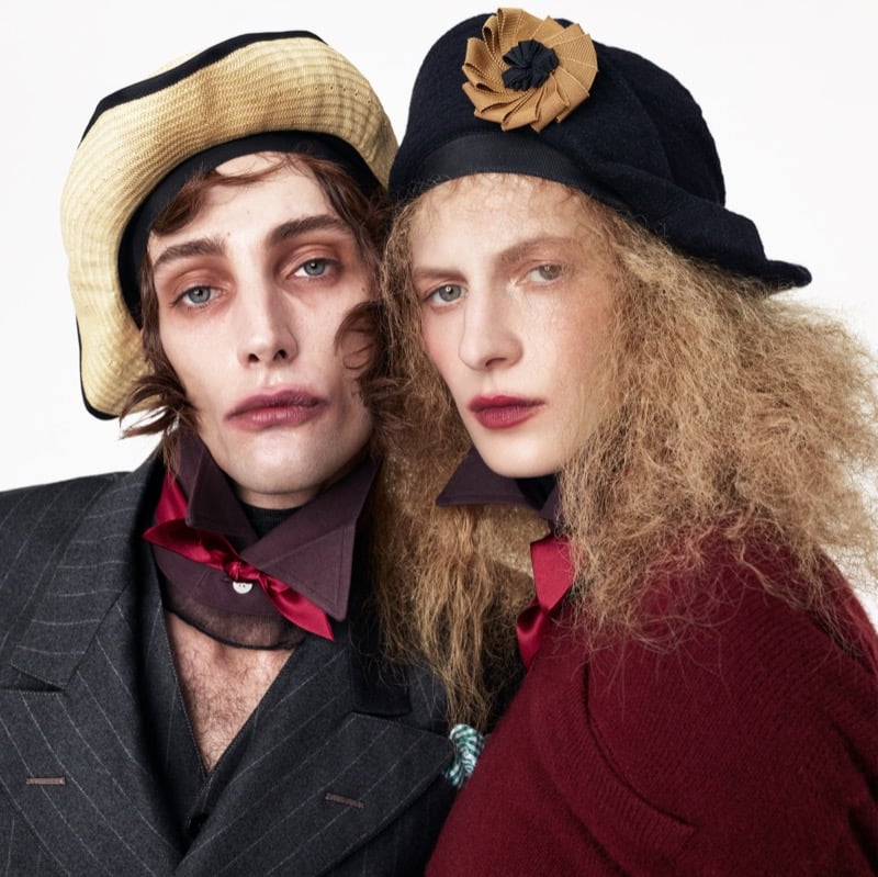 Close-up of Thomas Riguelle in a straw hat and pinstripe jacket beside Julia Nobis in a rosette-trimmed cap