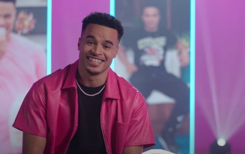Toby Aromolaran wears a pearl necklace with a black tee and open shirt on Love Island All Stars.