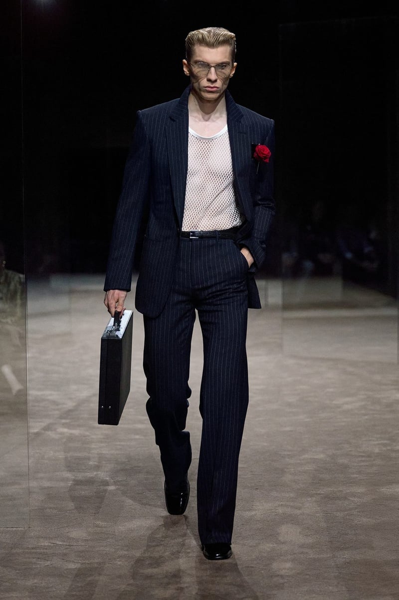 A model wears dark suit with an open pale shirt and a red rose at the breast pocket on the Tom Ford spring-summer 2027 runway.