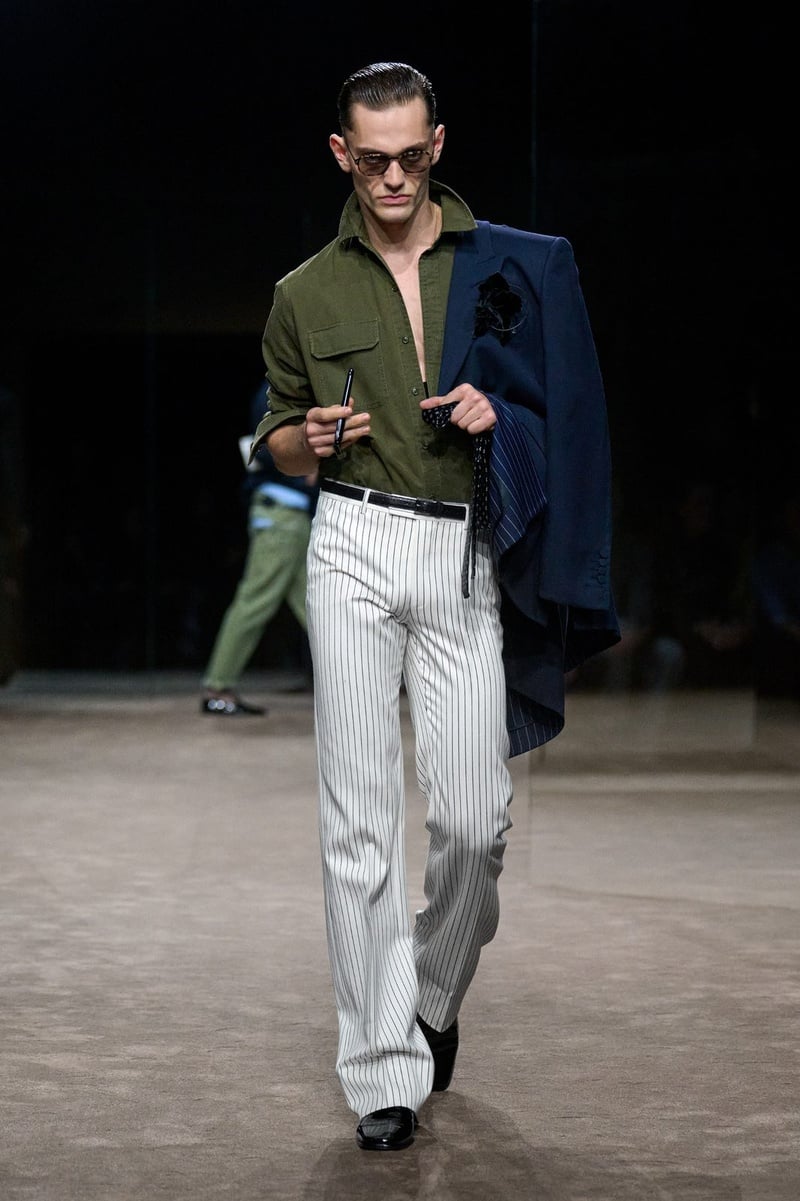 A model wears open olive shirt with pale trousers and a jacket carried over the shoulder on the Tom Ford spring-summer 2027 runway.
