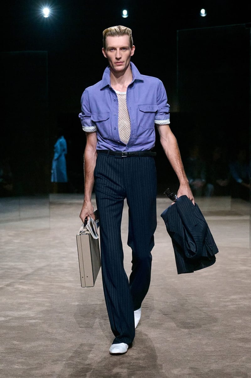 A model wears short-sleeved lavender shirt tucked into dark trousers, carrying a briefcase on the Tom Ford spring-summer 2027 runway.