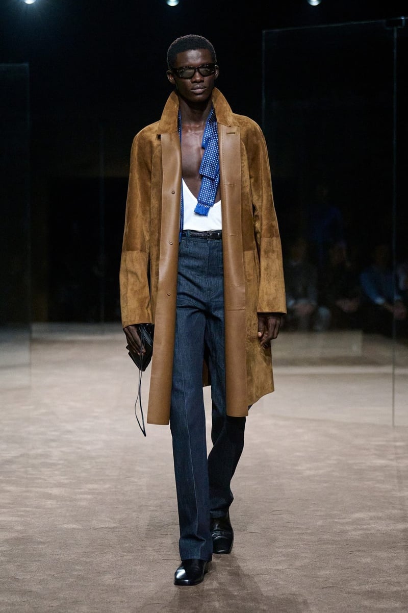 A model wears brown coat over an open shirt and dark trousers on the Tom Ford spring-summer 2027 runway.