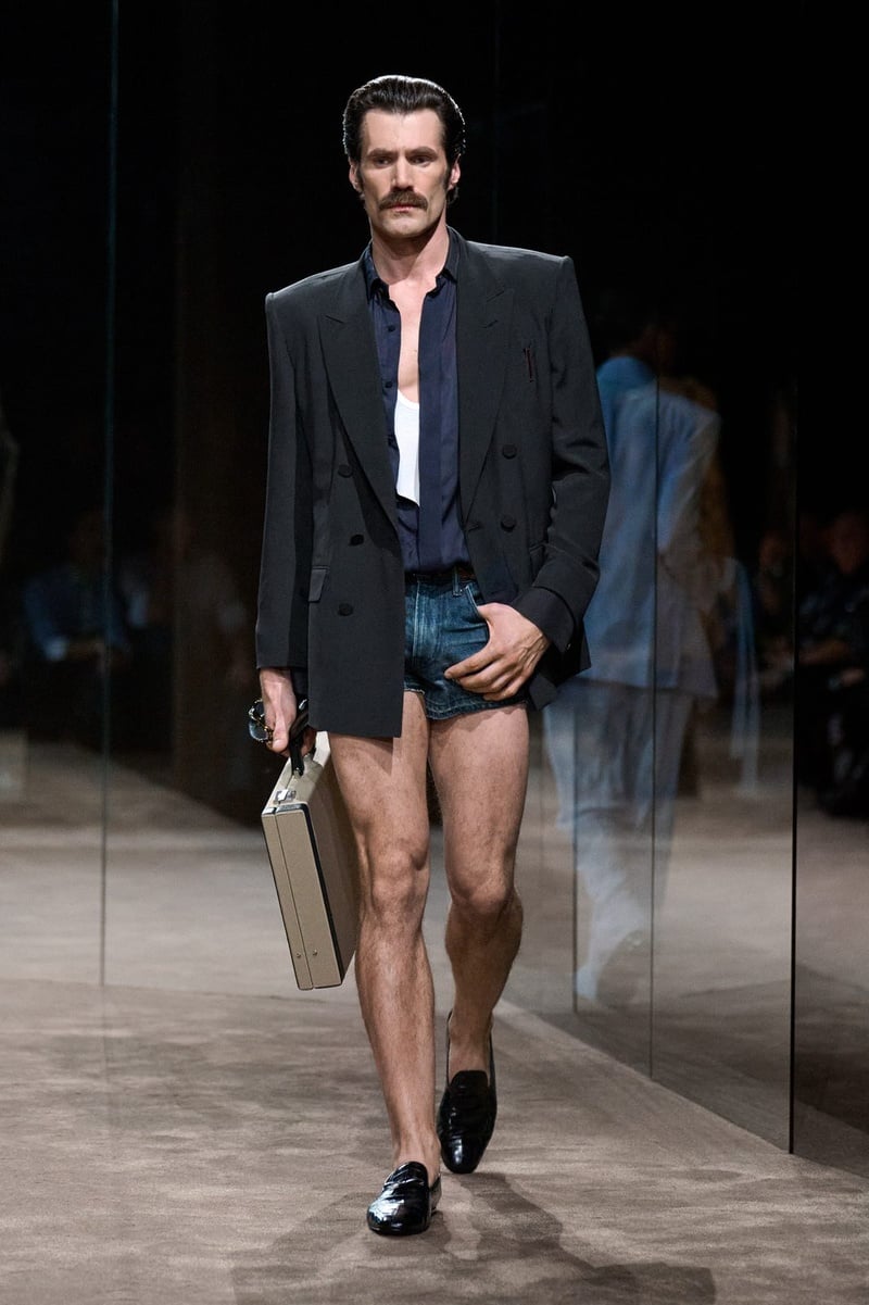 Darek Wierzycki wears double-breasted jacket over an open shirt and white tank with tiny denim shorts, carrying a briefcase on the Tom Ford spring-summer 2027 runway.