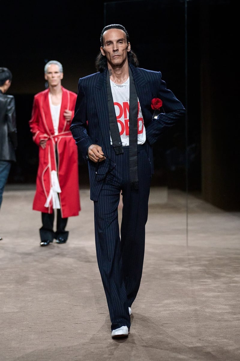 A model wears dark suit with a printed T-shirt and red rose on the Tom Ford spring-summer 2027 runway.