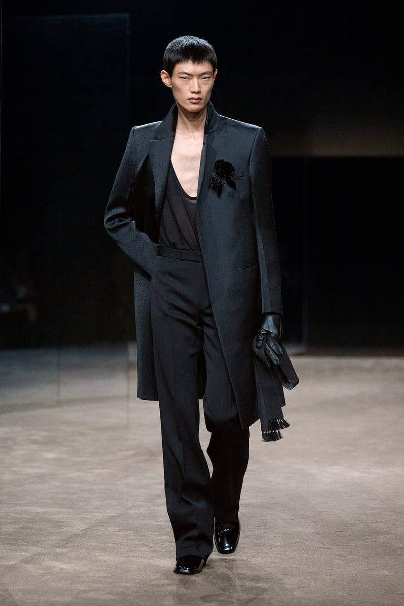 A model wears dark jacket over a deeply plunging black top and trousers on the Tom Ford spring-summer 2027 runway.