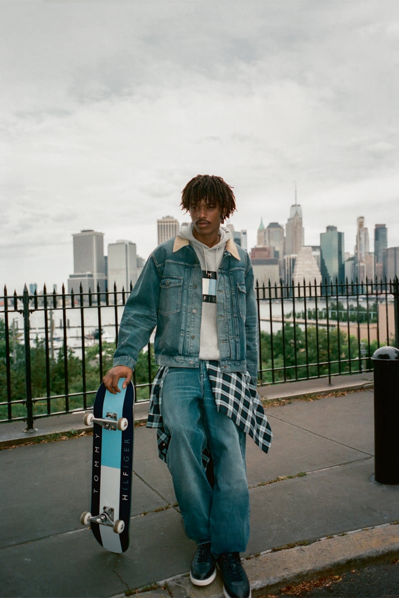 Nile Winchester carries a skateboard along the waterfront in a denim jacket and relaxed jeans.