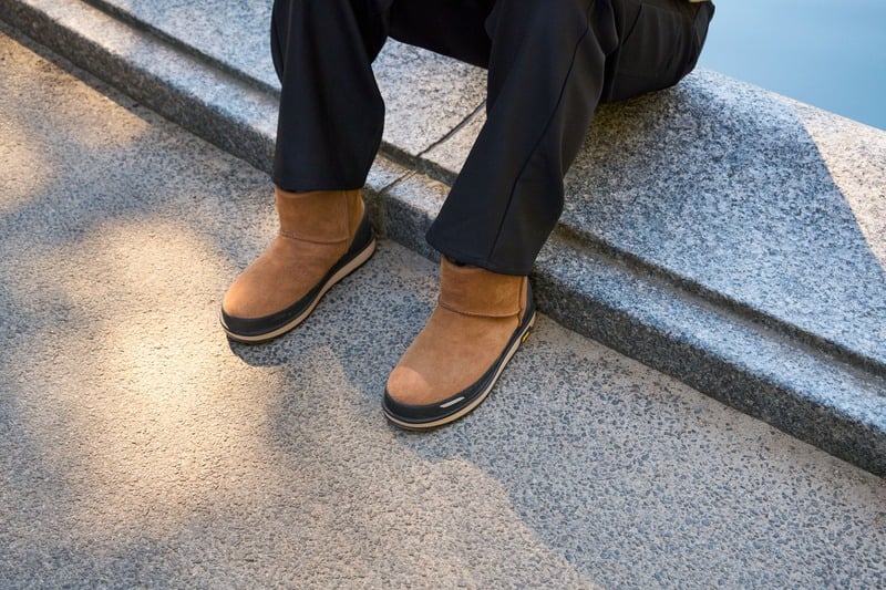 Dao-Yi Chow wears black trousers with chestnut UGG Classic Mini Guard GTX boots beside the water.