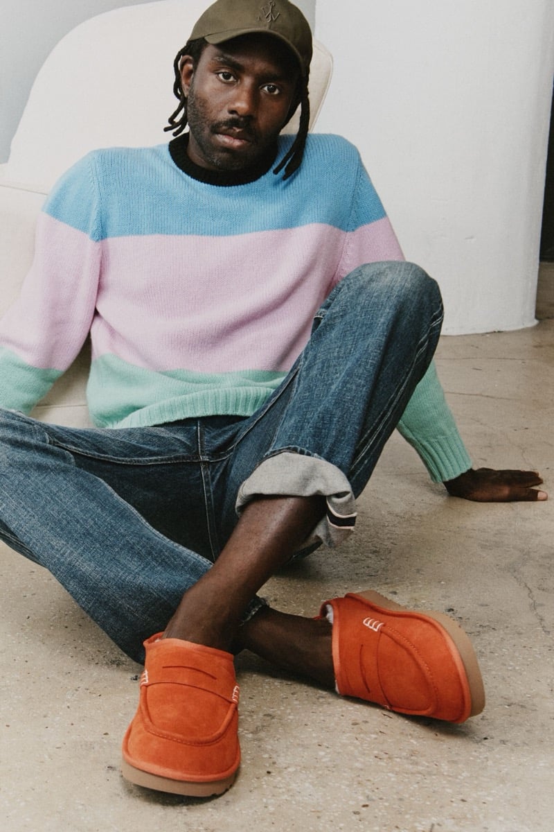 Dev Hynes sits on the floor in a pastel color-block sweater, rolled-up jeans, and Orange UGG x JW Anderson loafers.