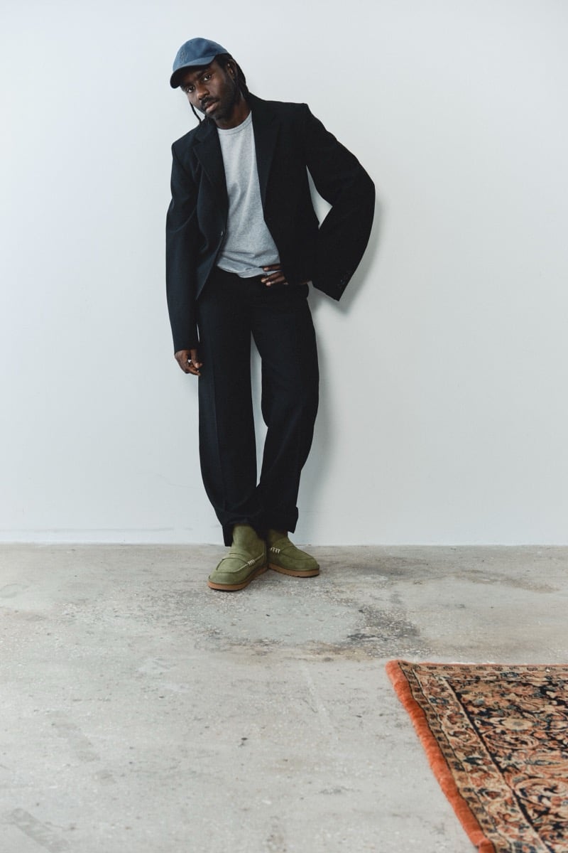 Dev Hynes wears black tailoring, a white T-shirt, and Khaki UGG x JW Anderson loafer boots.