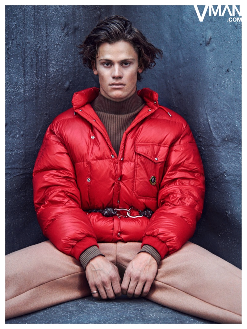 Lucas Pinheiro Braathen wears a red Moncler puffer jacket with a brown turtleneck and beige trousers.