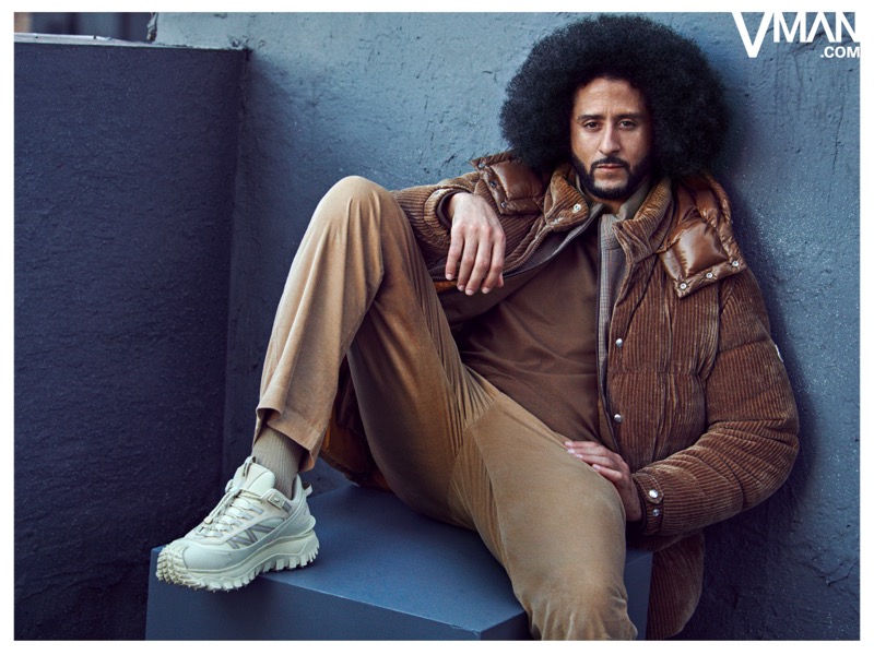 Colin Kaepernick reclines in a brown Moncler jacket, tan trousers, and light-colored sneakers.