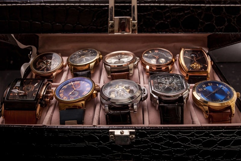 Ten wristwatches arranged on cushions inside an open black storage box.