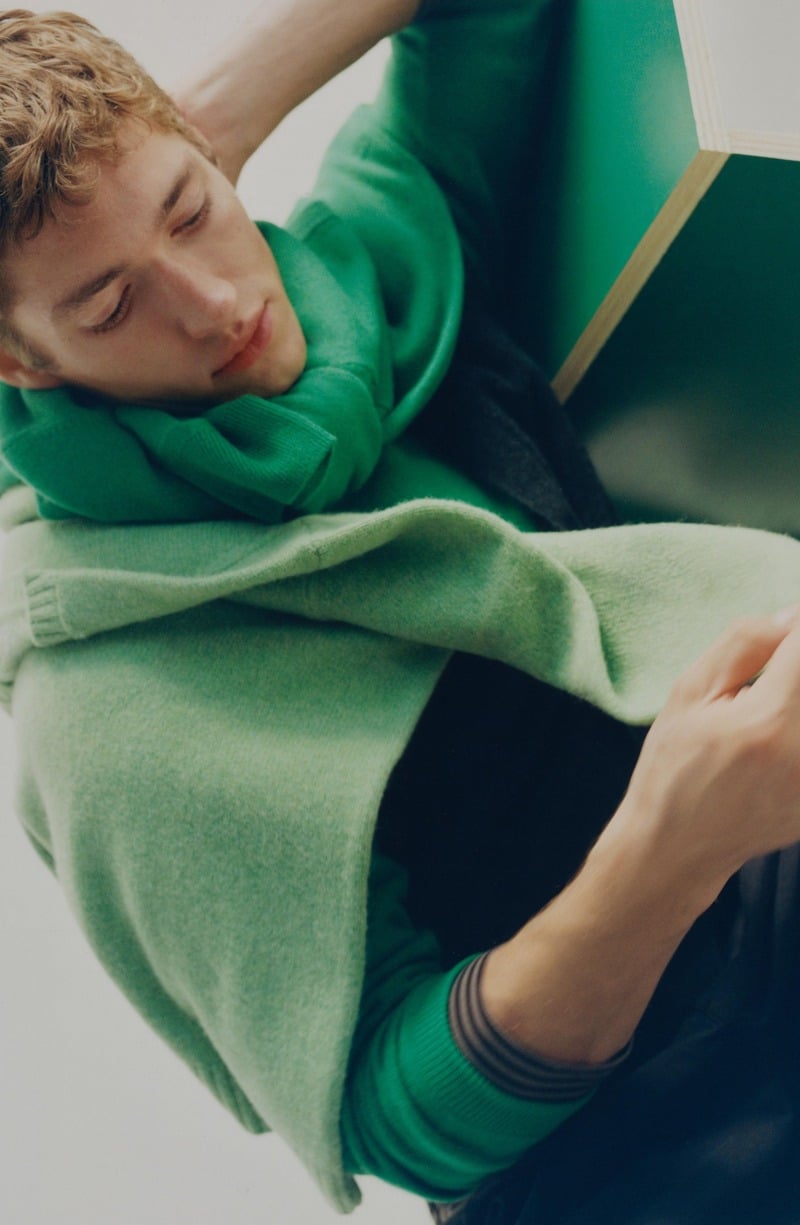 Valentin Humbroich reclines in layered green knitwear beside a green chair.