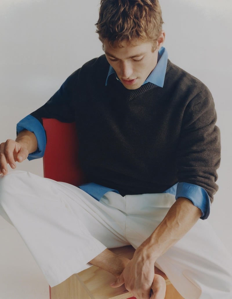 Valentin Humbroich looks down while seated in a dark sweater, blue shirt, and white trousers.