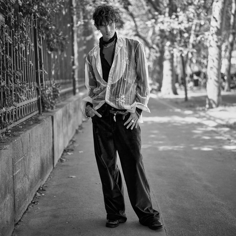 Cirillo wears a striped jacket over a dark knit with wide-leg trousers beside an ivy-covered fence for Zara Studio's fall-winter 2026 campaign