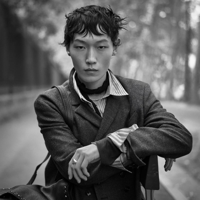 Li Cheng Yuan rests his arms on a bag wearing a tailored jacket over striped shirting for Zara Studio's fall-winter 2026 campaign