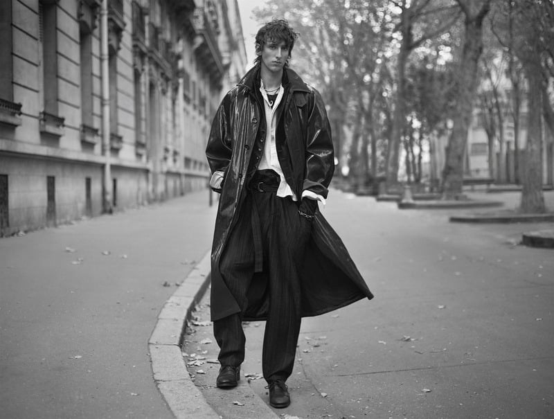 Luke Boyer wears a long leather coat over layered shirts and loose trousers on a tree-lined street for Zara Studio's fall-winter 2026 campaign